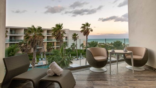 Ein Balkon mit Korbmöbeln, einem kleinen Tisch und Blick auf Strand und Palmen.