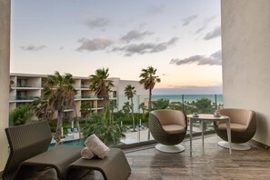 A balcony with wicker furniture, a small table, and a view of a beach and palm trees. - Grand Palladium Select Costa Mujeres - All Inclusive (Costa Mujeres)