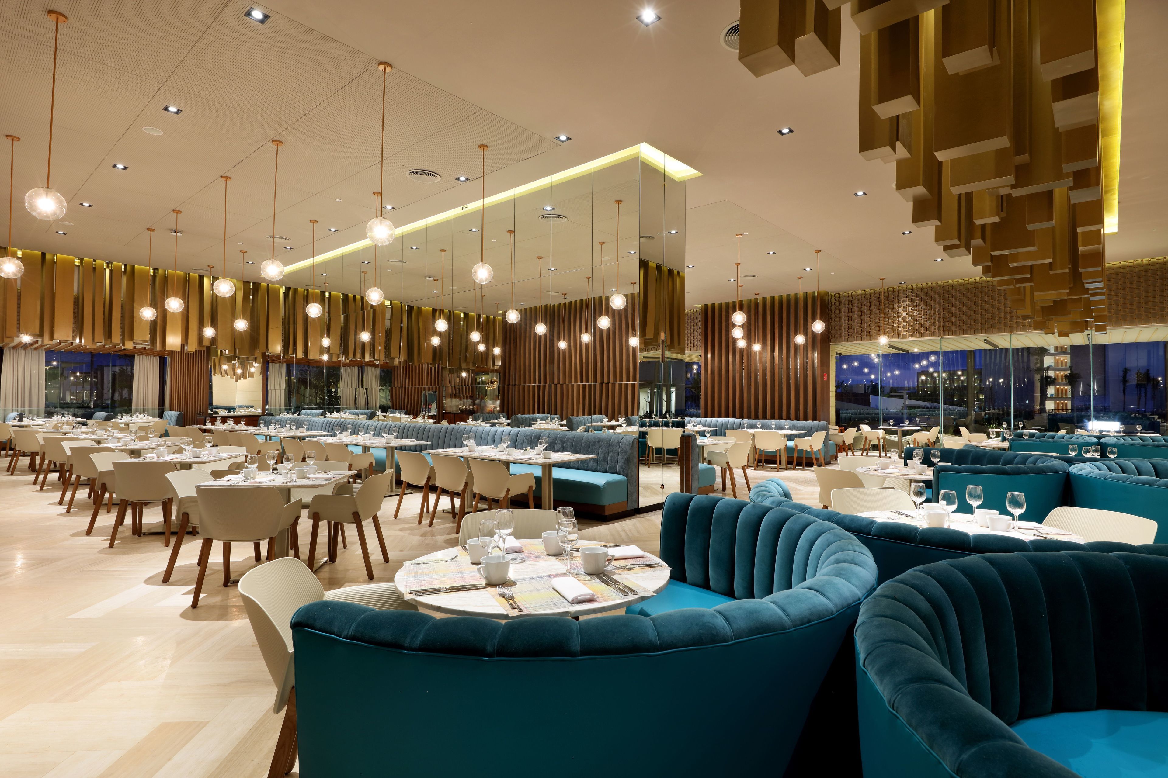 A modern restaurant with round tables, blue upholstered seating, and a high ceiling with hanging lights.