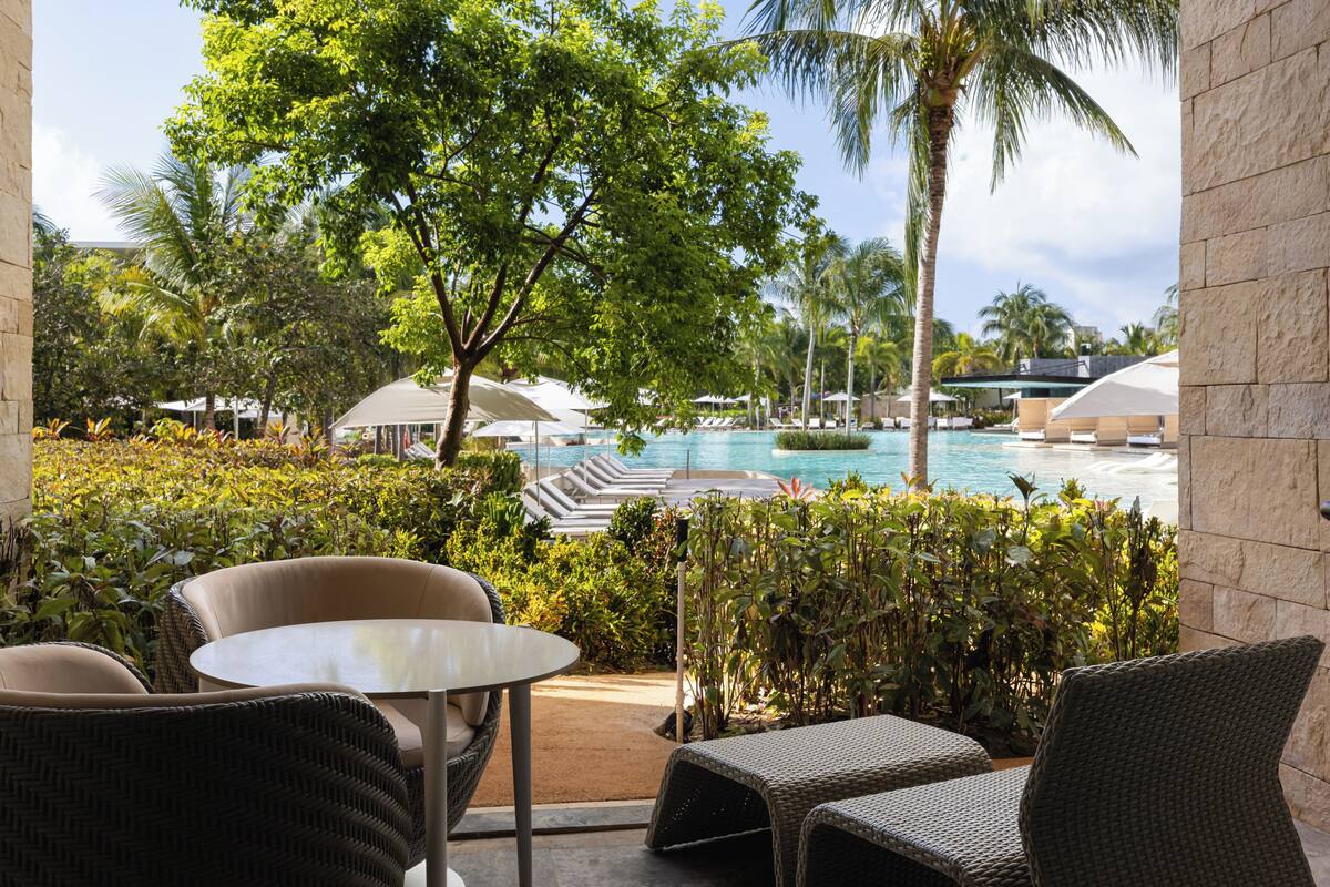 A resort patio with wicker furniture, a pool, and lush greenery.