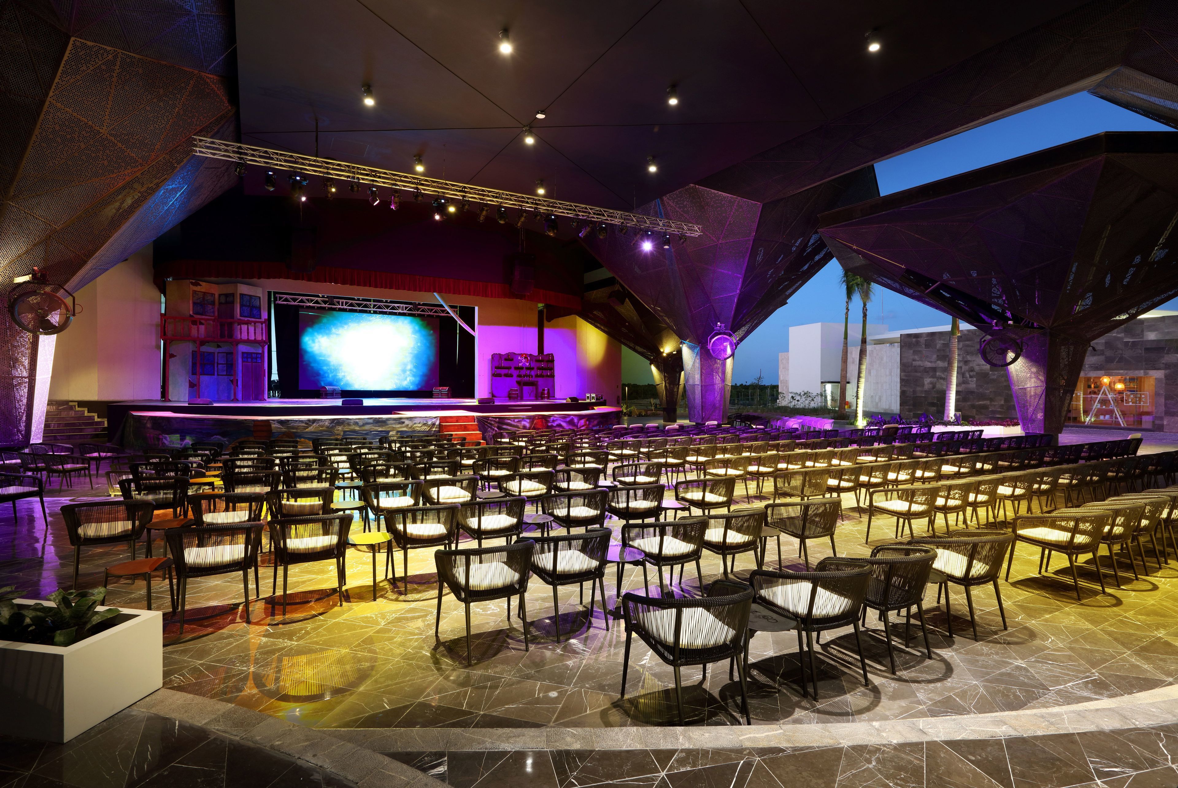 A spacious indoor venue with tiered seating, a large screen, and a stage.