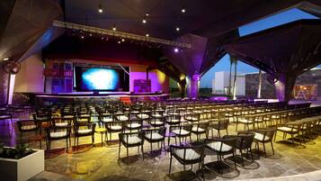 A spacious indoor venue with tiered seating, a large screen, and a stage.