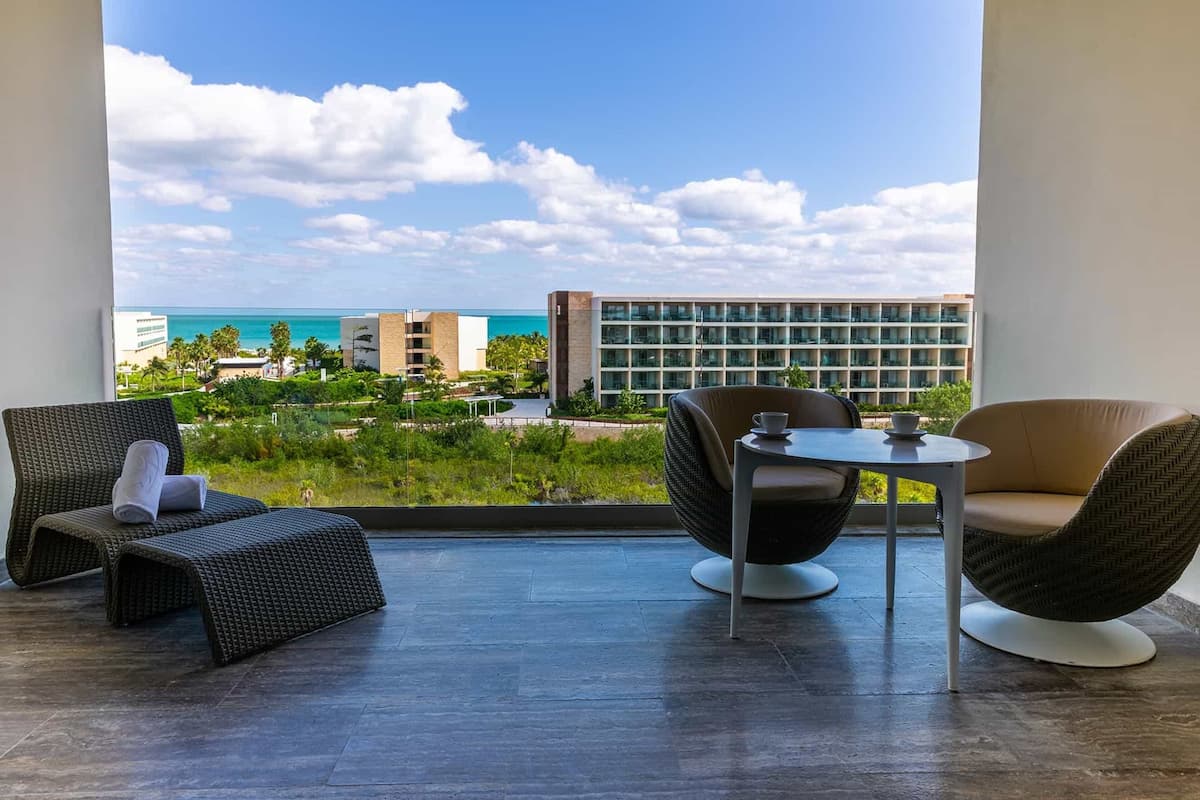 A balcony with wicker furniture, a small table, and a view of the ocean and buildings.