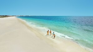 Ein weiter Sandstrand mit klarem türkisblauem Wasser.