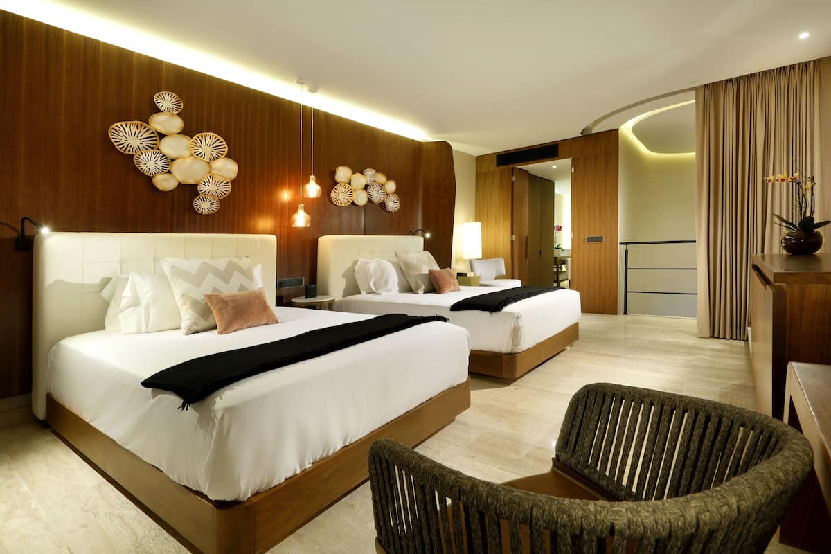 A hotel room with two beds, a sitting area with a chair, and a wooden wall with decorative panels.