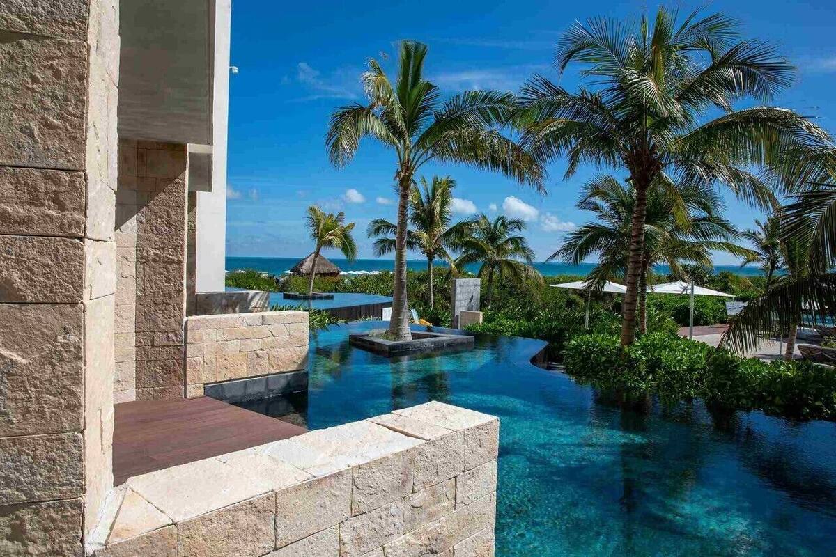 A pool area with clear blue water, surrounded by palm trees and a view of the ocean.