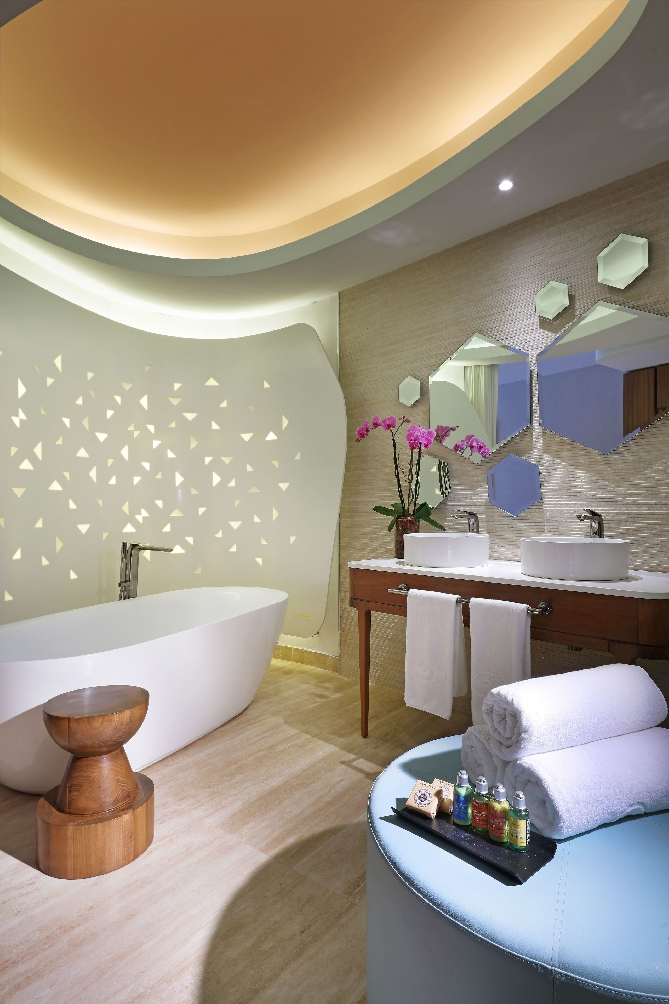 A modern bathroom with a freestanding bathtub, a vanity with two sinks, and a wooden stool.