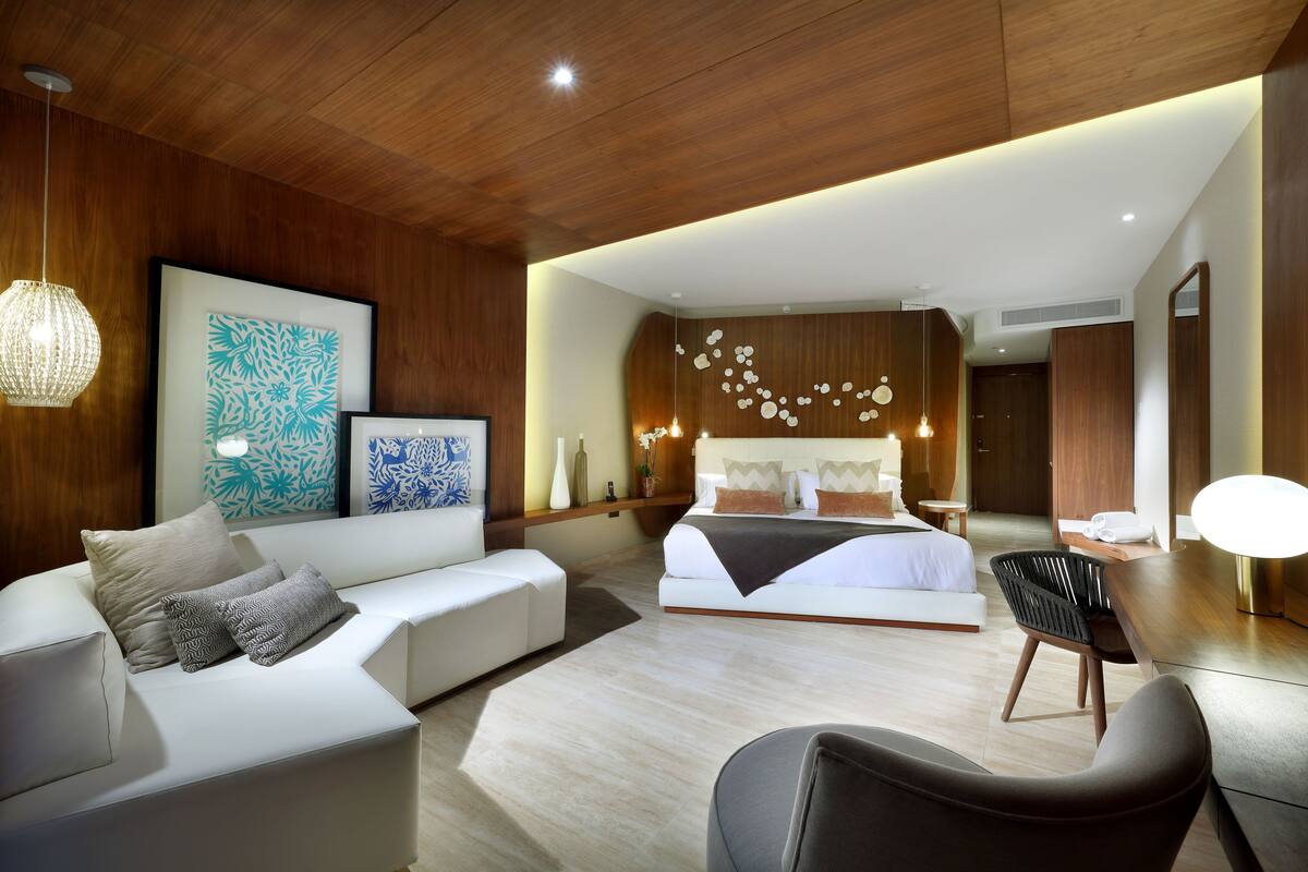 A modern bedroom with a large bed, a sitting area with a sofa, and a dining table.