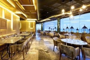 Un restaurante con varias mesas y sillas, piso de mármol pulido y vistas amplias a través de grandes ventanales.