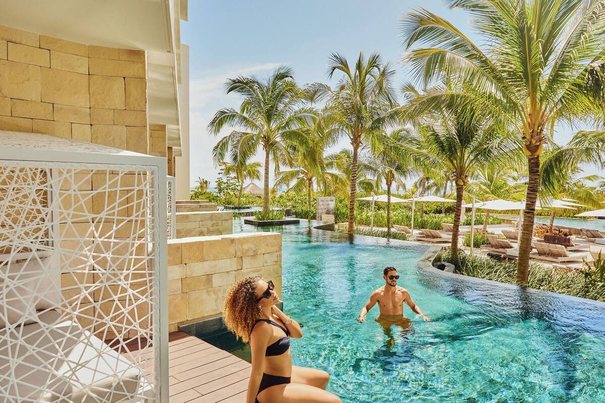 A pool area with clear water, palm trees, and a white structure.