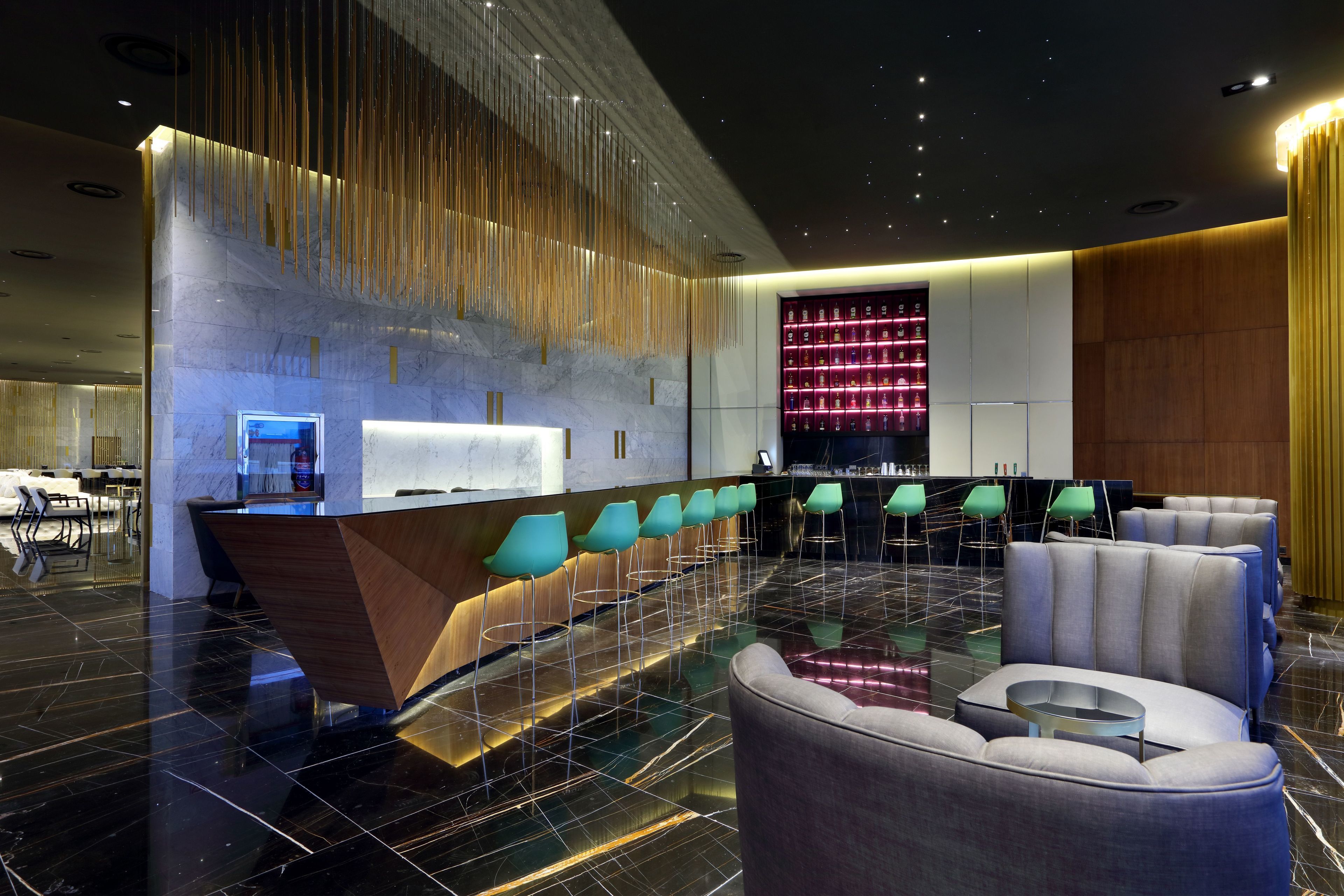 A modern lobby with a reception desk, bar area, seating, and a decorative wall.