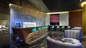 A modern lobby with a reception desk, bar area, seating, and a decorative wall.
