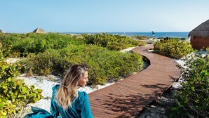 A wooden pathway leading to a beach area with a thatched-roof structure.