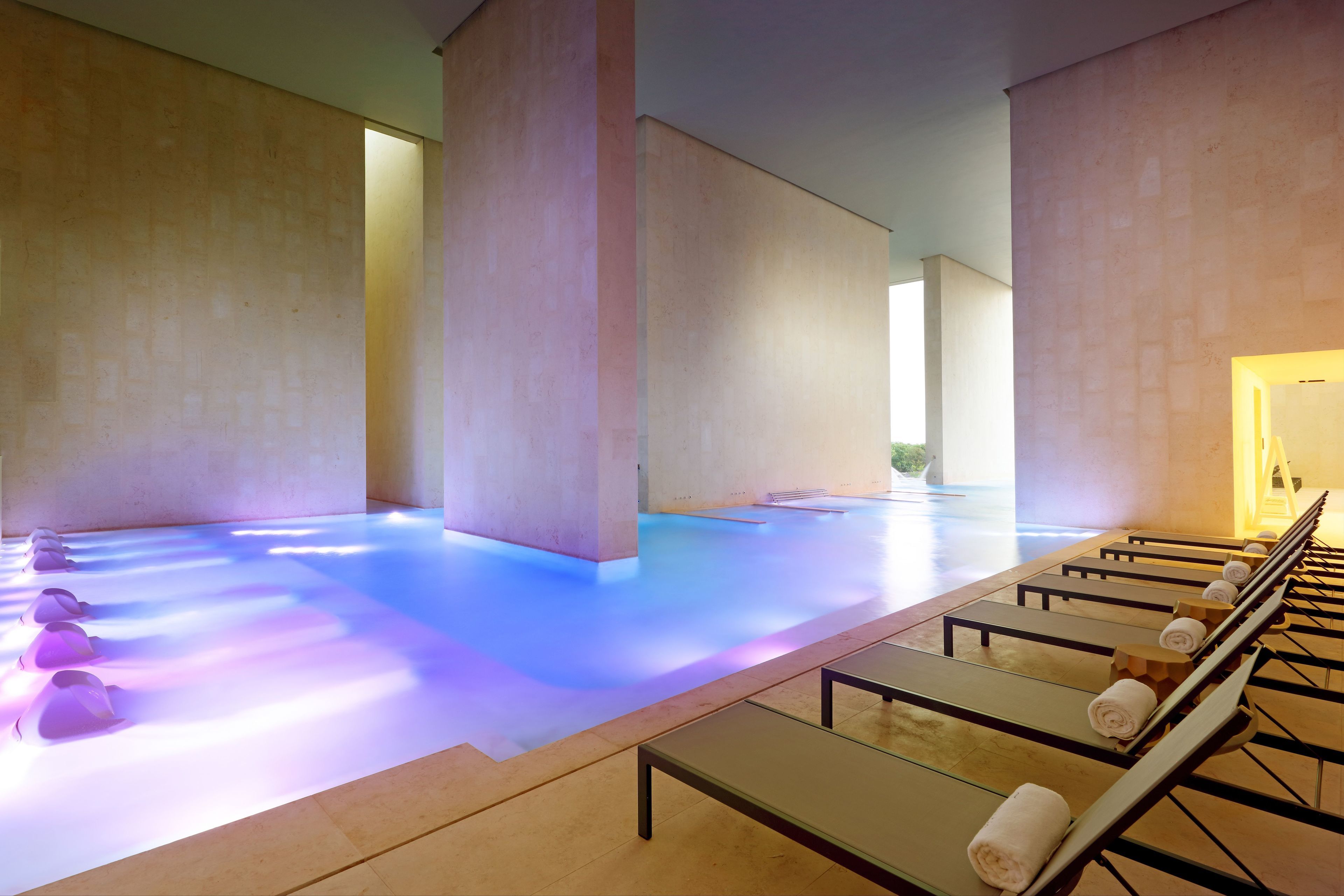 Un espacio de spa con suelo calefaccionado, tumbonas y un largo banco con toallas.