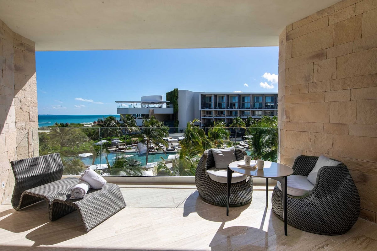 A balcony with wicker furniture, a pool, and a view of a resort building.