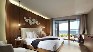 A modern hotel room with a large bed, a desk, and a view of the ocean.