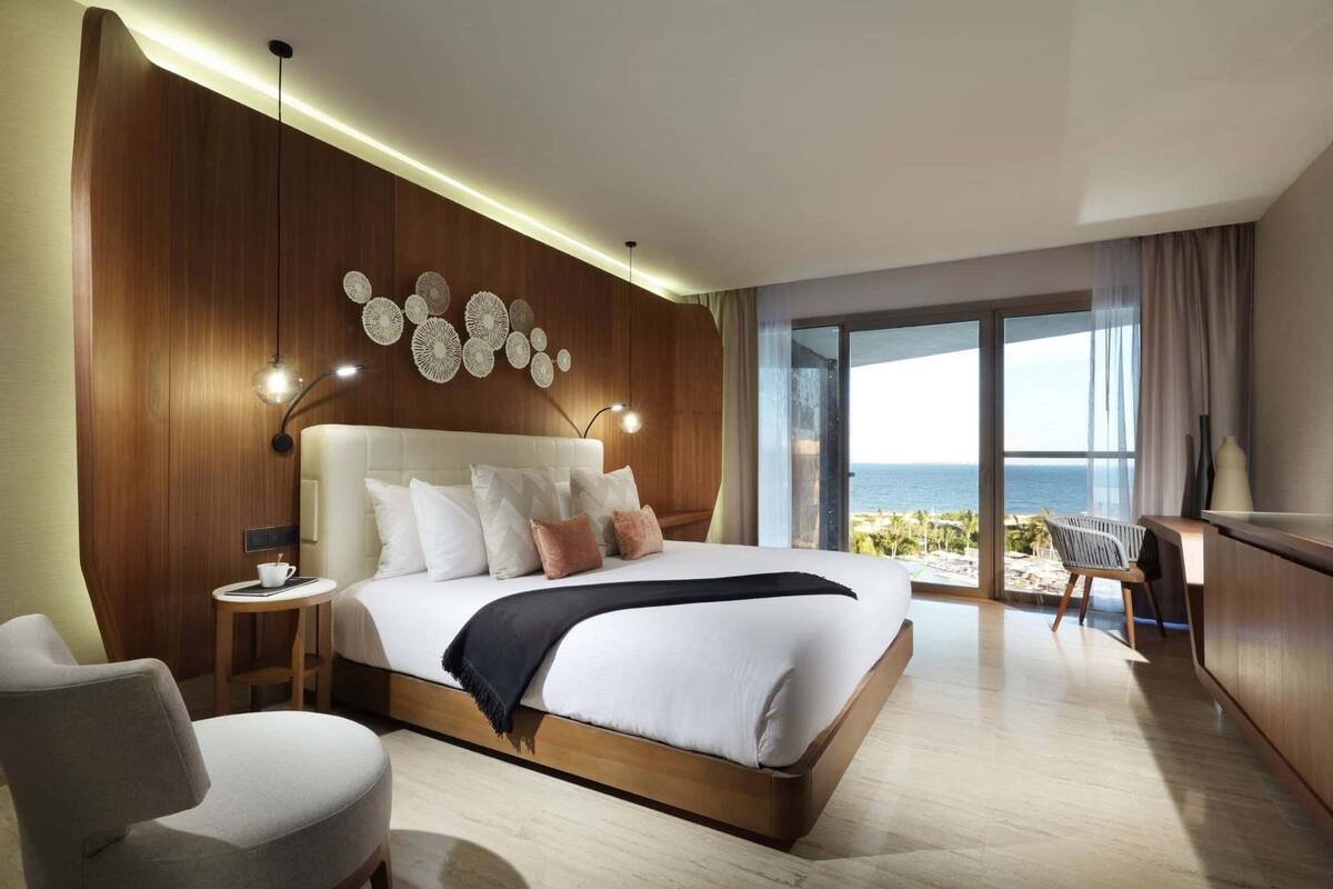 A modern hotel room with a large bed, a desk, and a view of the ocean.