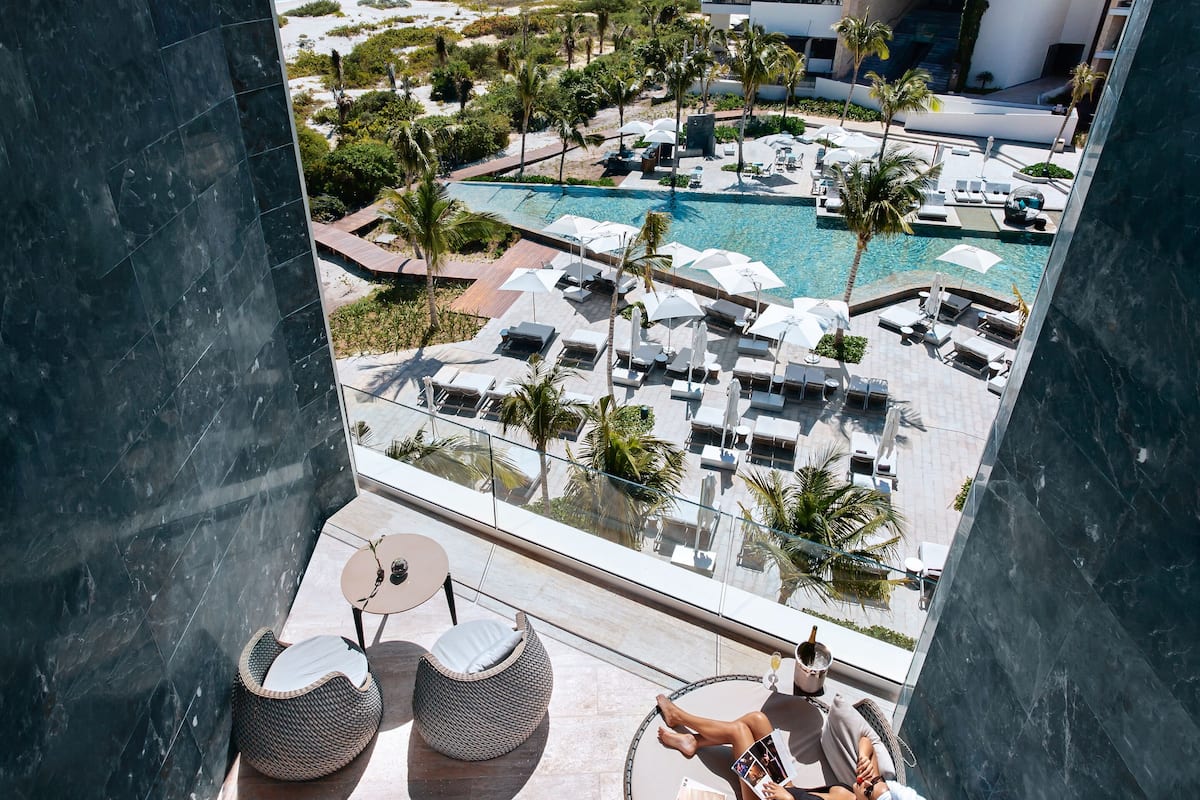 A balcony with a view of a pool area, lounge chairs, and a small hot tub.