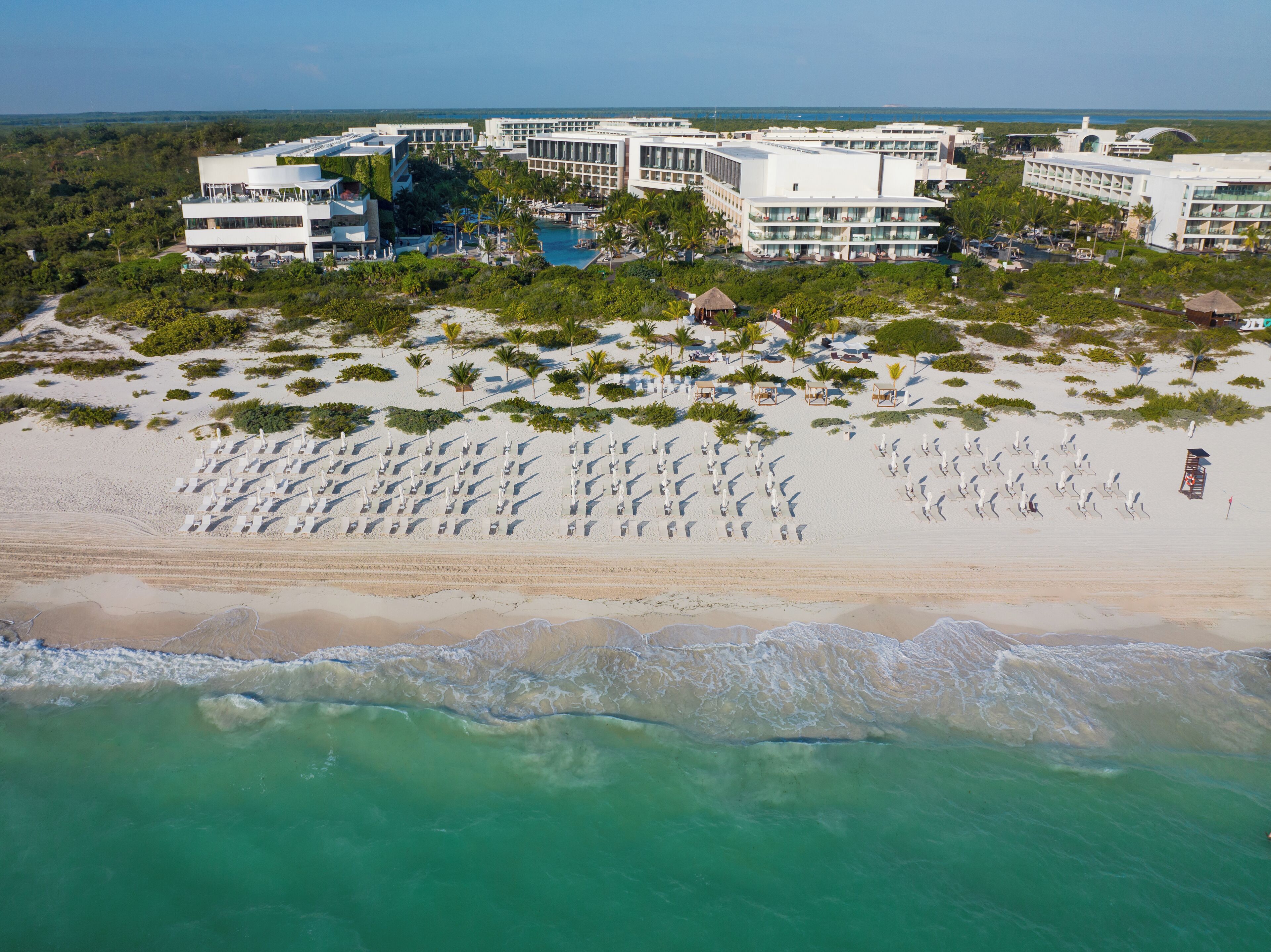 A resort with multiple buildings, a beach with sun loungers, and a pool area.