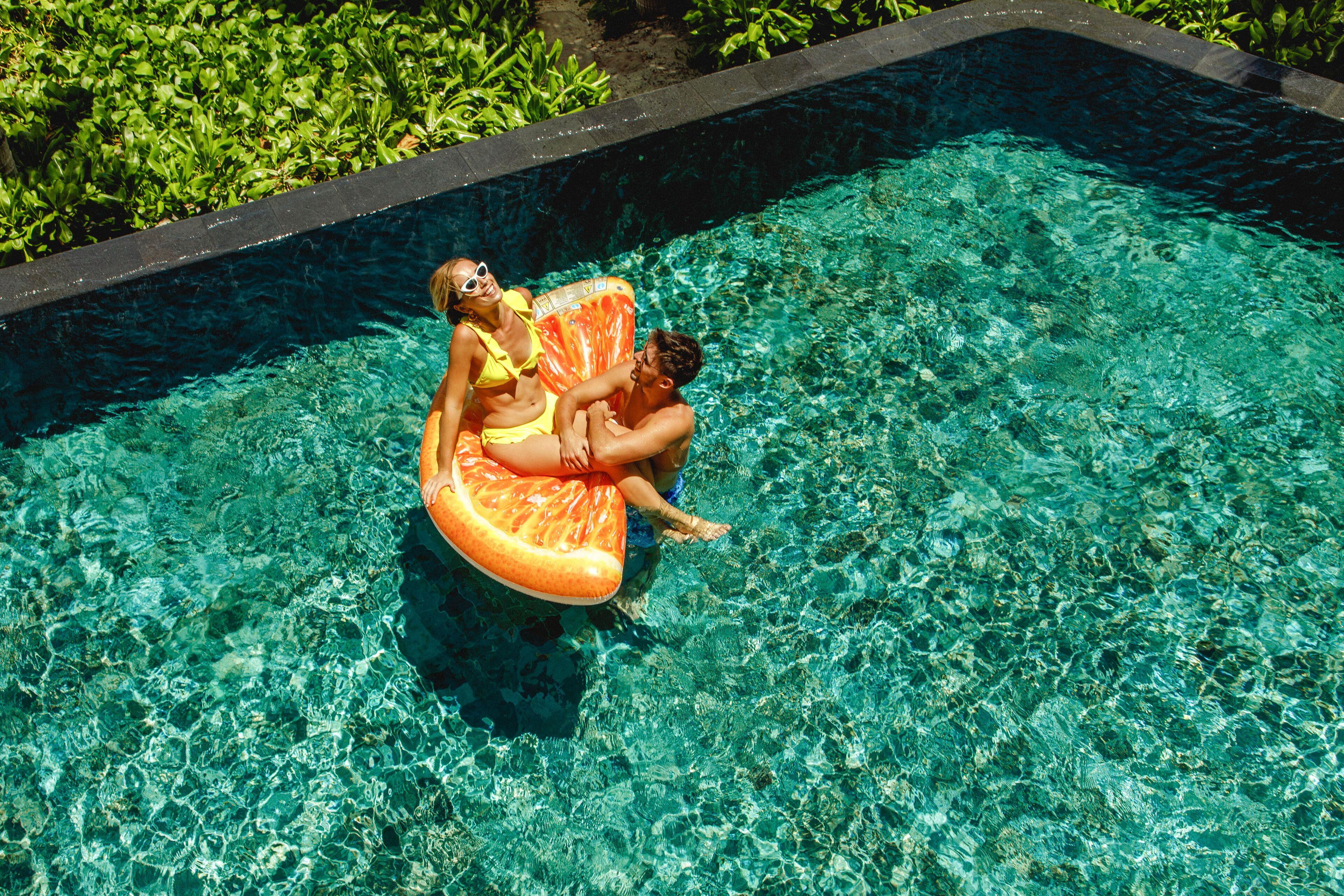 Una piscina con agua cristalina y una persona sentada en un flotador naranja.
