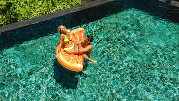 Una piscina con agua cristalina y una persona sentada en un flotador naranja.