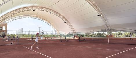 An indoor tennis court with a high, arched roof and multiple lighting fixtures.