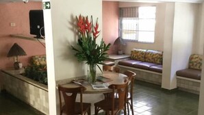 A dining area with a round table and chairs, a vase with flowers, and a bench with cushions in the background. - Hotel Porto Grande (Maceió)