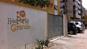 A hotel entrance with a large sign reading "Hotel Porto Grande" and a gated parking area with parked cars. - Hotel Porto Grande (Maceió)