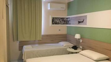 Habitación de hotel con dos camas individuales, una mesita con lámpara y aire acondicionado instalado en la pared.