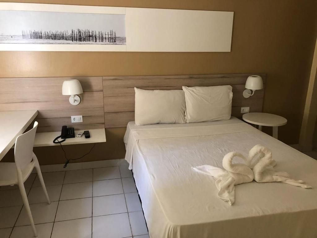 A hotel room with a bed, bedside lamps, a desk with a phone, and a wall-mounted artwork.