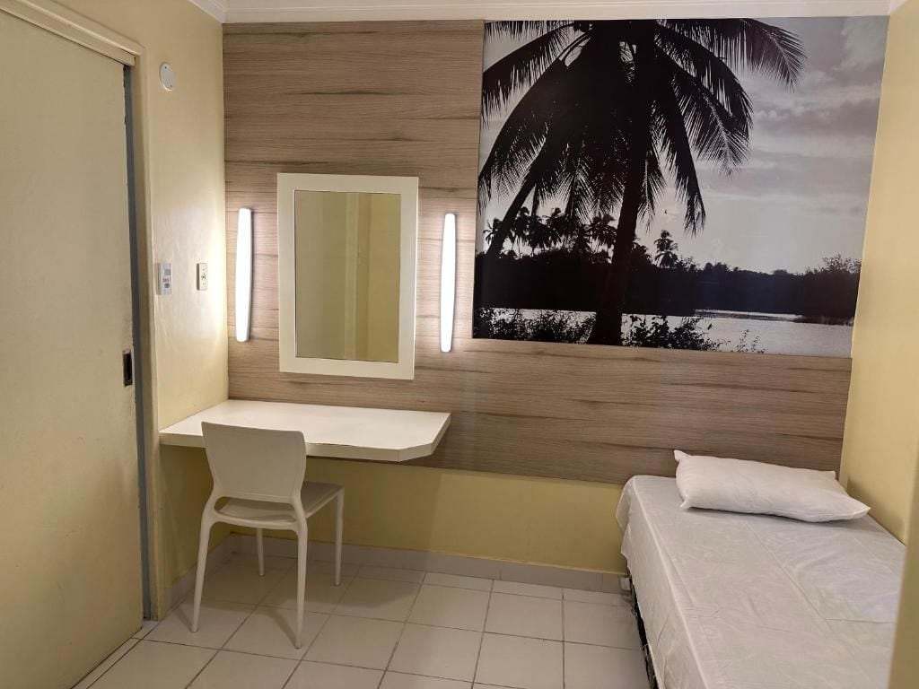 Ein Zimmer mit einem Bett, einem Schreibtisch, einem Stuhl, einem wandmontierten Spiegel und einer großen Wandmalerei von Palmen.