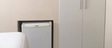 A room with a bed, a TV mounted on the wall, a wardrobe, and a small refrigerator.