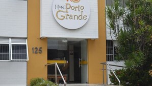The exterior of Hotel Porto Grande, featuring a prominent circular sign with the hotel name, a yellow and white facade, and a visible entrance with a glass door. - Hotel Porto Grande (Maceió)