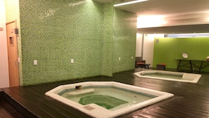 Ett spaområde med två bubbelpooler på ett trädäck, omgivet av gröna mosaikväggar.