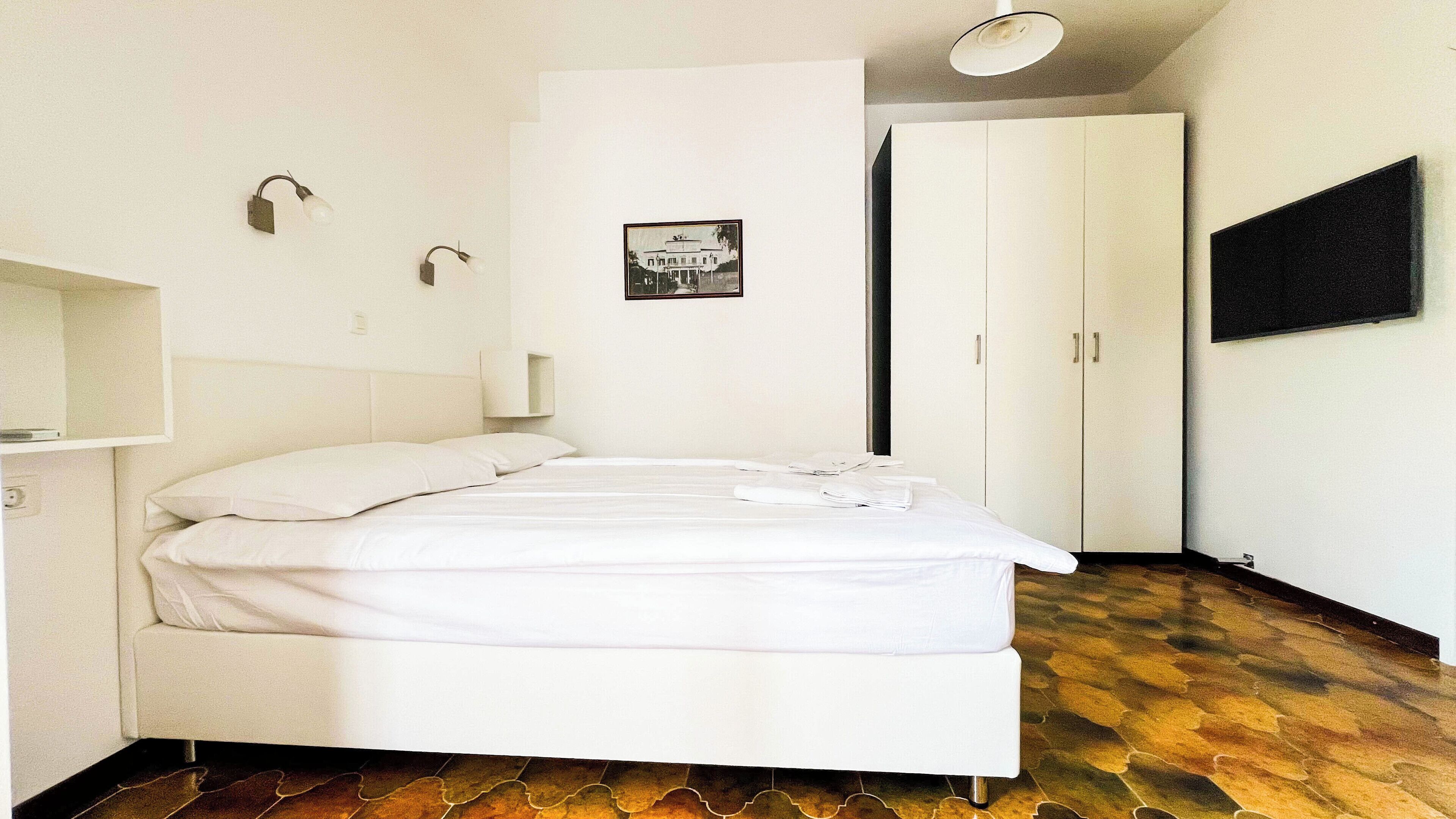 A bedroom with a bed, a wardrobe, a TV, and a framed picture on the wall.
