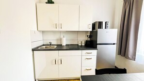 A compact kitchen with white cabinets, a black countertop, a stainless steel sink, a coffee machine, and a refrigerator. - Rooms Koblar (Piran)