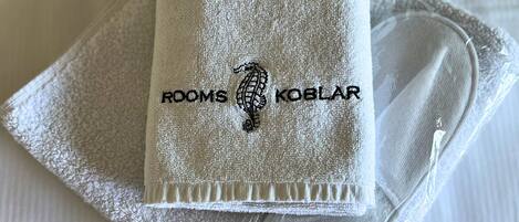 A neatly folded white towel with embroidered text and a seahorse design, placed on a white surface.