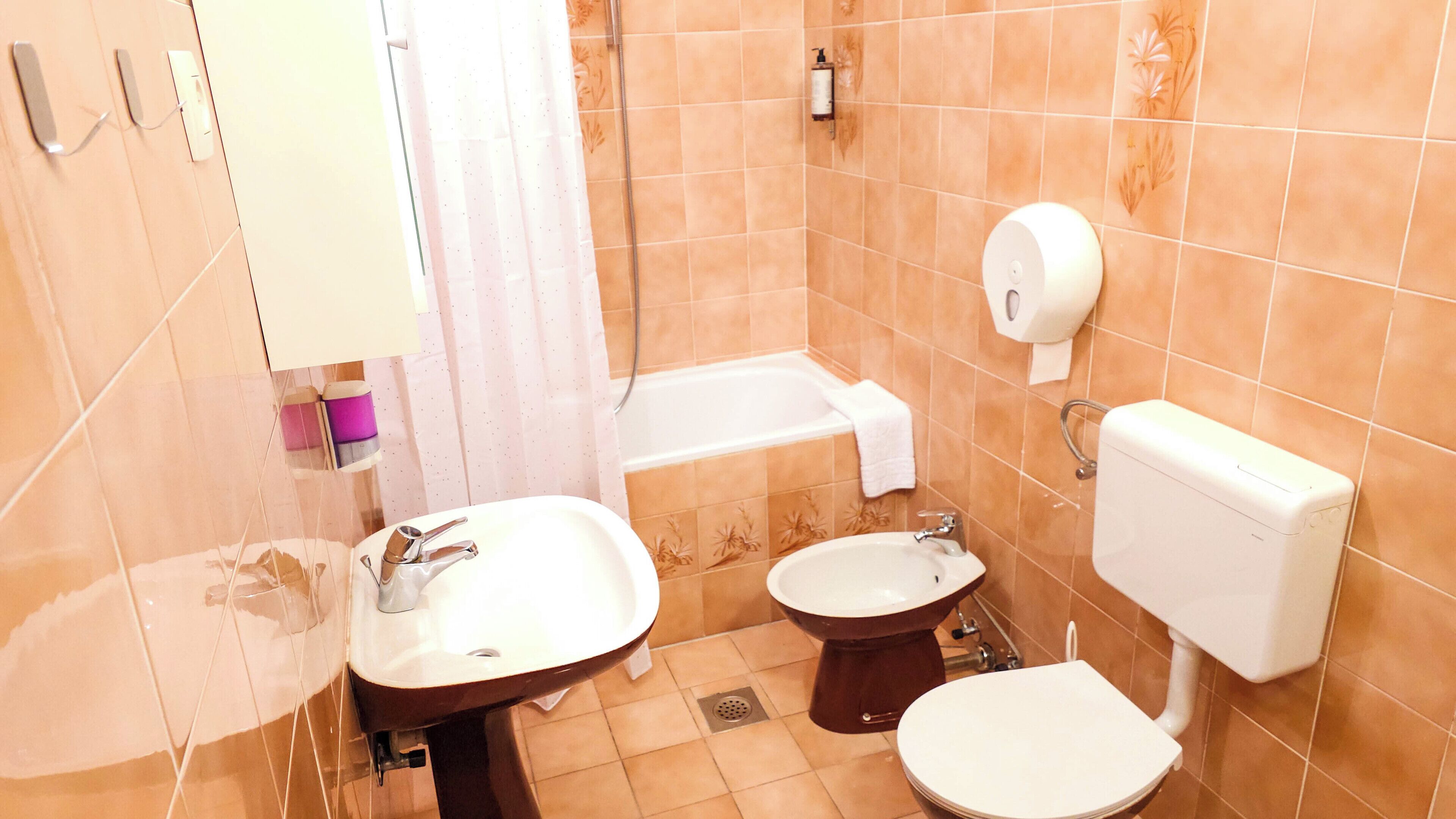 A bathroom with a bathtub, two sinks, a toilet, and a hand dryer.