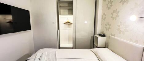 A hotel room with a bed, a TV mounted on the wall, a wardrobe, and a small bedside table with a tissue box.