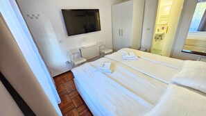 A hotel room with a bed, a TV, a desk with a chair, and a bathroom visible through a glass door. - Rooms Koblar (Piran)