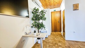 A hallway with a wooden floor, a white reception desk, a potted plant, and a wooden door with a sign above it. - Rooms Koblar (Piran)