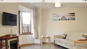 Een woonkamer met een open haard, een bank, een bijzettafeltje en een schilderij aan de muur.
