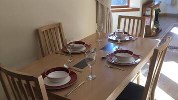 A dining table set with red and white plates, glasses, and cutlery, surrounded by wooden chairs with black cushions.
