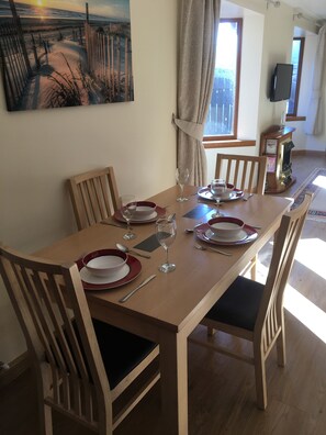 A dining table set with red and white plates, glasses, and cutlery, surrounded by wooden chairs with black cushions.