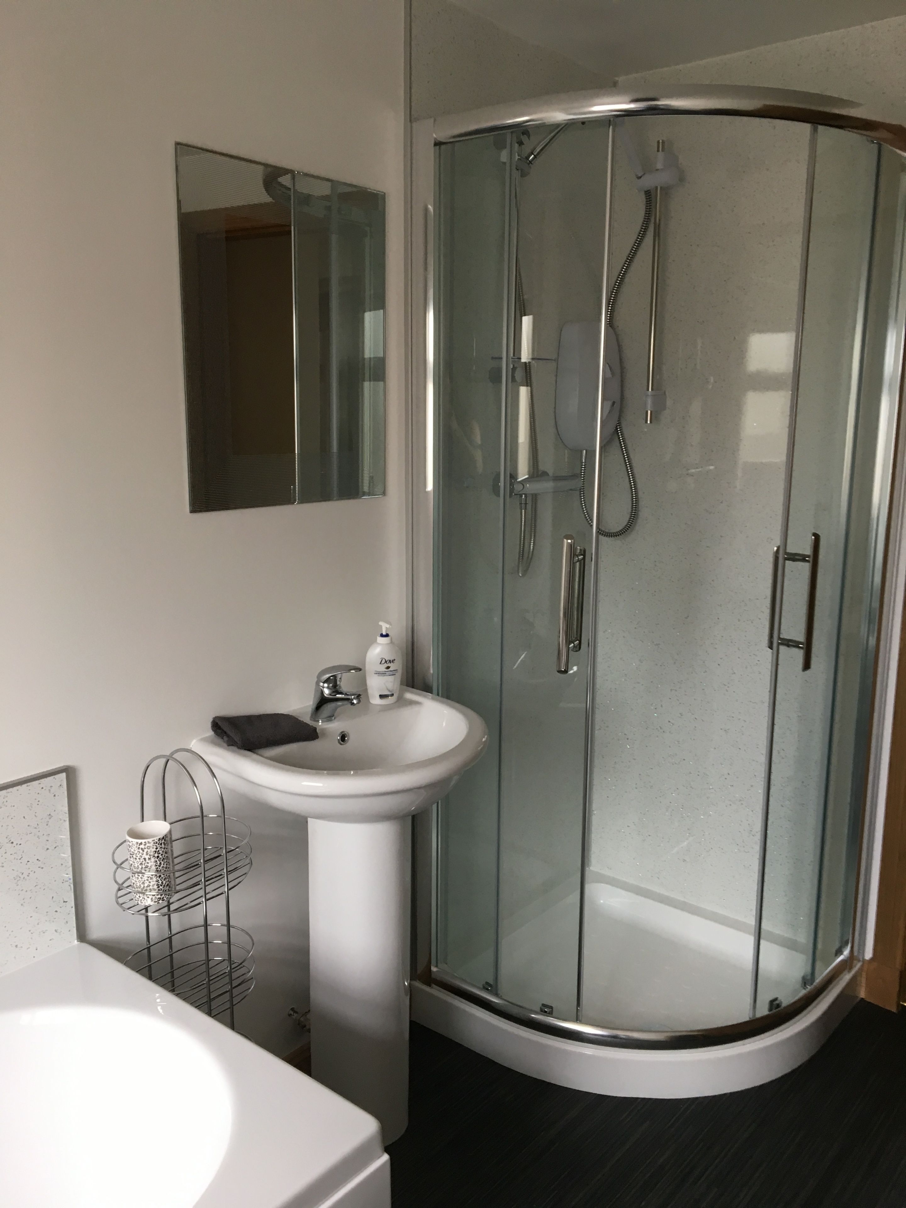 A modern bathroom with a glass-enclosed shower, a white sink, and a mirror above the sink.