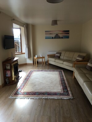 A living room with a beige sofa, a patterned rug, a wooden coffee table, and a television mounted on the wall.