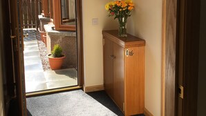 Een gang met een houten kast, een vaas met bloemen en uitzicht op een tuin.