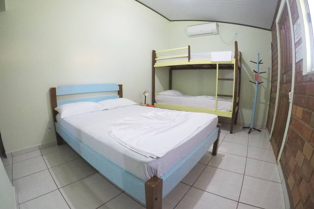Une chambre avec un lit superposé, un lit simple, une table de chevet, une lampe et un climatiseur fixé au mur.