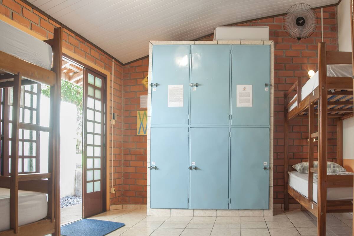 Une chambre avec des lits superposés, une armoire bleue et une porte donnant sur l’extérieur.