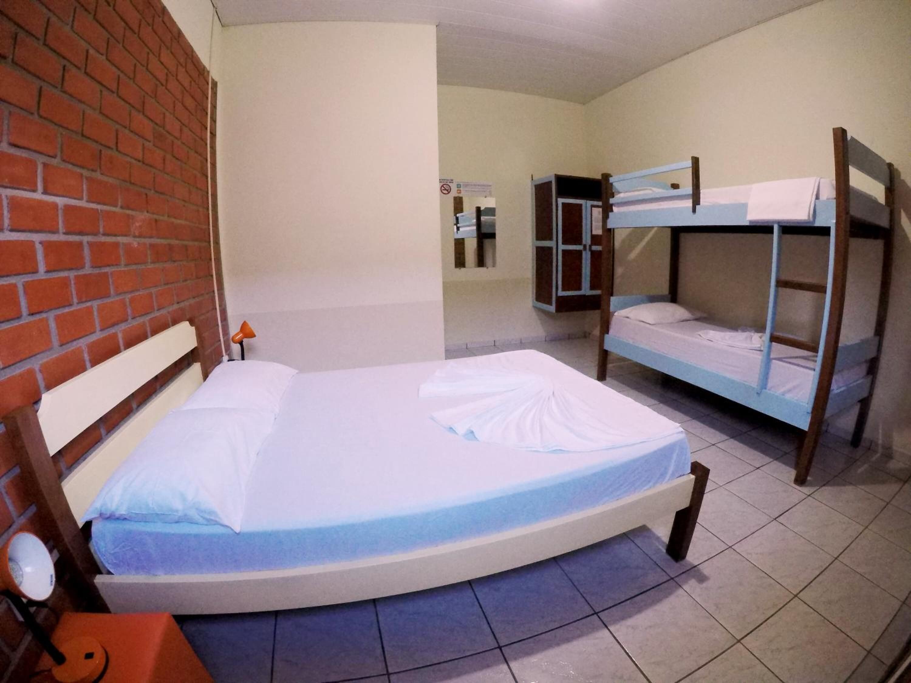 A room with a single bed, a wooden bunk bed, a brick wall, and a tiled floor.